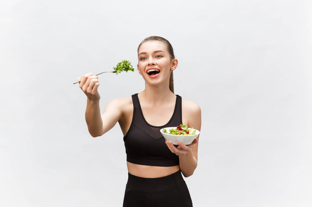 Giovane bella donna sportiva mangiare insalata su sfondo bianco. - Foto, immagini