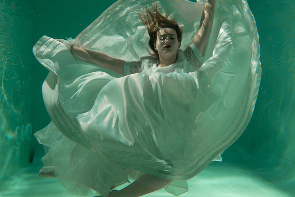 Hot Slim Caucasian Woman Posing Under water in beautiful clothes alone in the deep - Foto, Imagem