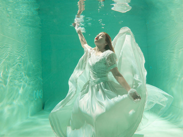 Kuuma hoikka valkoihoinen nainen poseeraa veden alla kauniissa vaatteissa yksin syvällä
 - Valokuva, kuva