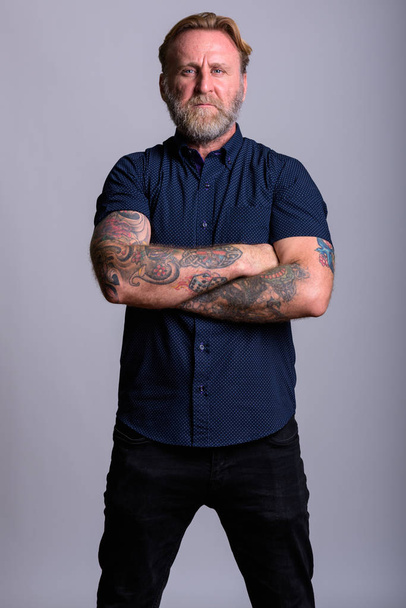 Studio shot of mature bearded man with hand tattoos standing wit - Photo, Image