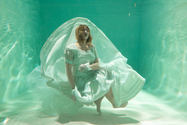 Hot Slim Caucasian Woman Posing Under water in beautiful clothes alone in the deep - Photo, Image