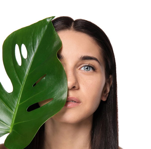 Portrait of beautiful young woman with natural makeup and tropical leaf on white background - Fotó, kép