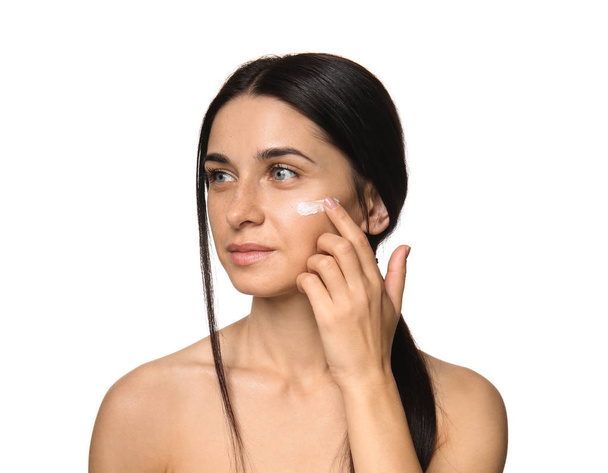 Portrait of beautiful young woman applying facial cream on white background - Zdjęcie, obraz
