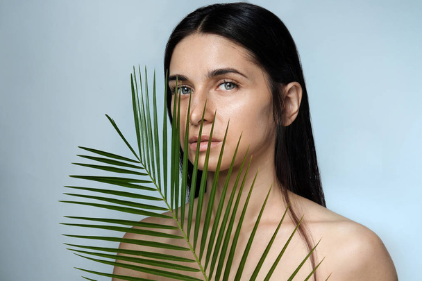 Portrait of beautiful young woman with natural makeup and tropical leaf on color background - Foto, immagini