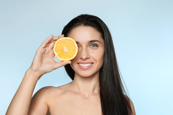 Portrait of beautiful young woman with natural makeup and orange on color background - Fotó, kép