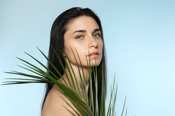 Portrait of beautiful young woman with natural makeup and tropical leaf on color background - Photo, Image