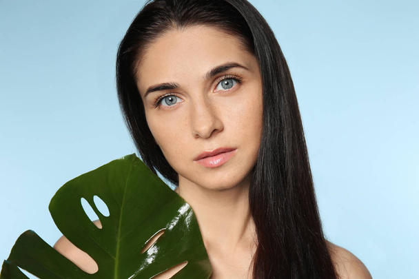 Portrait de belle jeune femme avec maquillage naturel et feuille tropicale sur fond de couleur
 - Photo, image