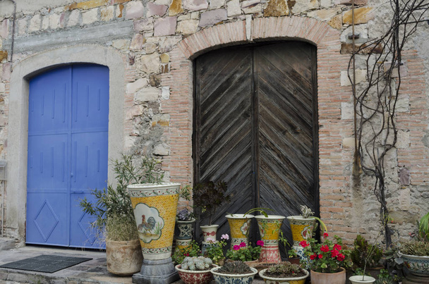 Παλιό κτίσμα με τοίχους από τούβλο, ξύλινες πόρτες και λουλούδια και φυτά σε διακοσμητικά βάζα και γλάστρες στην είσοδο. Λεπτομέρειες και στοιχεία της σχεδιασμό σπίτι διακόσμηση και τοπίο  - Φωτογραφία, εικόνα