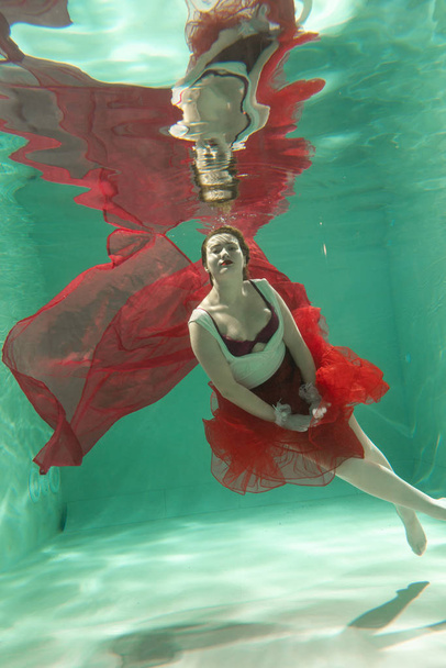 Hot Slim Caucasian Woman Posing Under water in beautiful clothes alone in the deep - Photo, Image