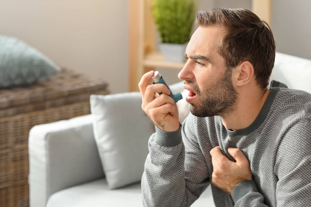 Hombre joven con inhalador que tiene un ataque de asma en casa - Foto, Imagen
