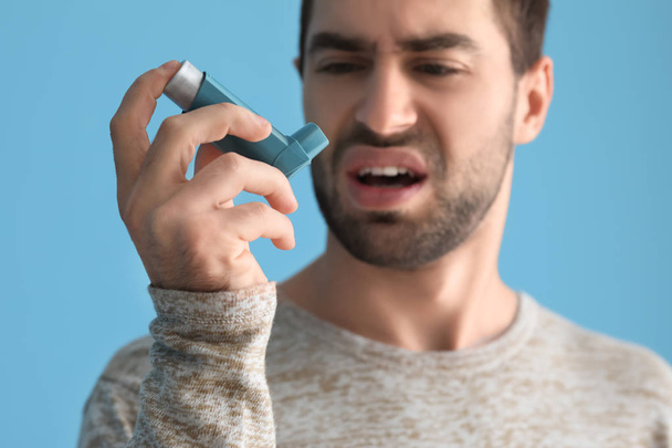 Young man with inhaler having asthma attack on color background - Photo, Image