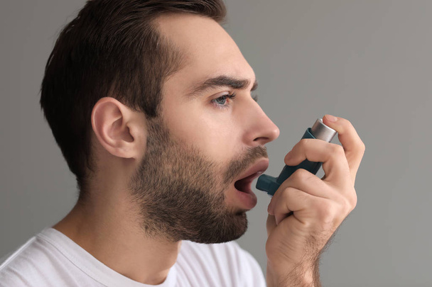 Młody człowiek z inhalatora o ataku na szarym tle astmy - Zdjęcie, obraz