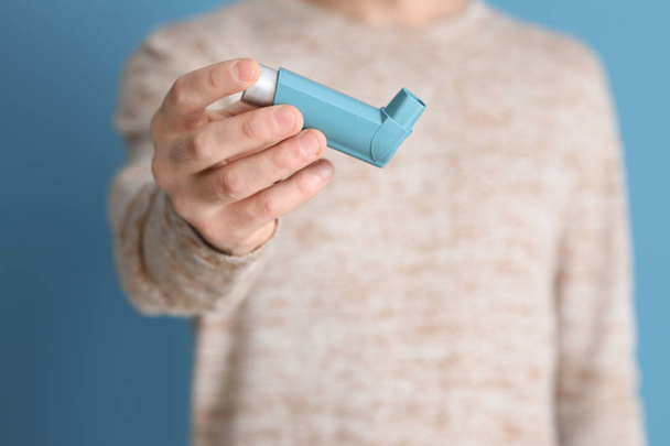 Young man with inhaler on color background, closeup - Foto, Bild