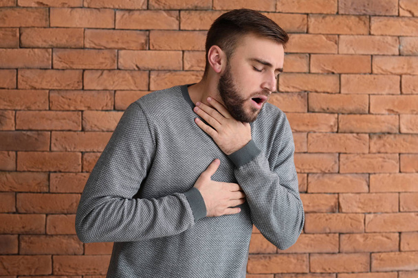 Junger Mann mit Asthmaanfall gegen Ziegelwand - Foto, Bild