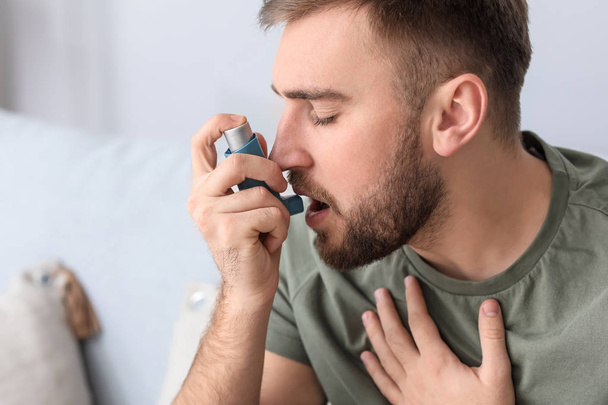 Young man with inhaler having asthma attack at home - Valokuva, kuva