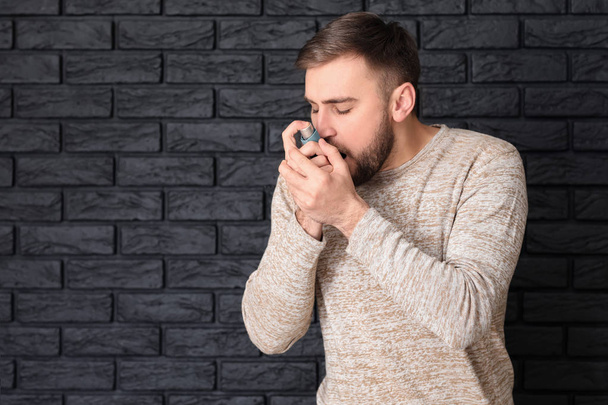 Young man with inhaler having asthma attack on dark background - Photo, Image