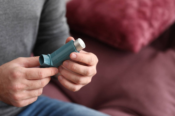 Young man with inhaler at home, closeup - Foto, afbeelding