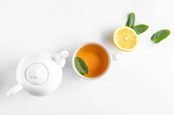 Teapot, cup of hot beverage, lemon and mint on white background - Fotó, kép