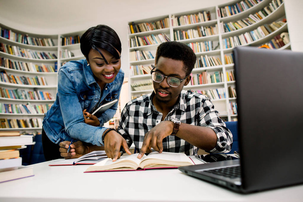 University students african boy and girl sitting together at table with books and laptop. Happy young people doing group study in library. Academic Library Student Learning Concept - Fotografie, Obrázek