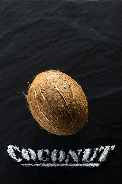 Целый спелый кокос на черном текстурном фоне, крупный план и вид сверху
 - Фото, изображение
