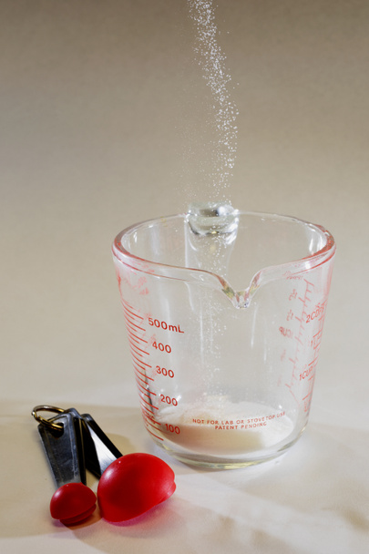 Detenga la vista en movimiento del azúcar de caña blanca haciendo pucheros en una taza de medir
. - Foto, imagen