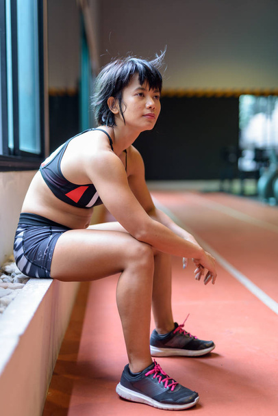 Fiatal gyönyörű ázsiai nő ül, és pihentető az edzőteremben - Fotó, kép