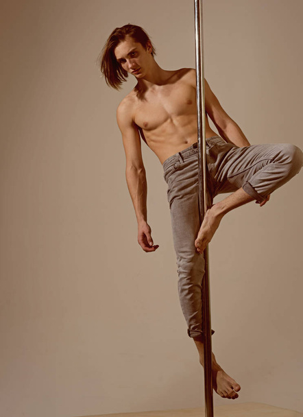 Pole dance trainer. Young man training on pylon in grey studio - Zdjęcie, obraz