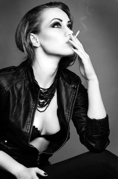 A portrait of beautiful sexual redheaded girl is in a black leather jacket, smoking a cigarette - Foto, afbeelding