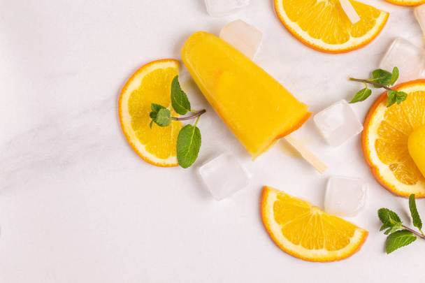 Homemade orange popsicle with ripe orange and fresh mint on light marble background. Healthy desserts. Lactose free ice cream. - Foto, imagen