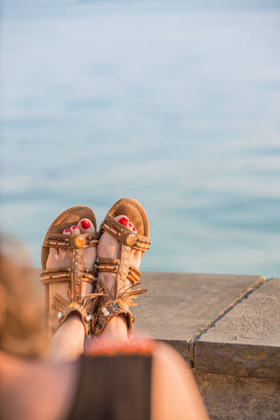Młoda kobieta spoczywa jej nogi w skórzane sandały na brzegu morza - Zdjęcie, obraz
