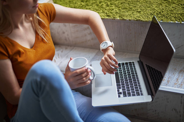 Cropped portrait of charming girl checking the time while sitting on steps with laptop and holding cup of coffee - Fotó, kép