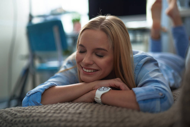Joyful blond girl in blue shirt lying on couch at home - Fotó, kép