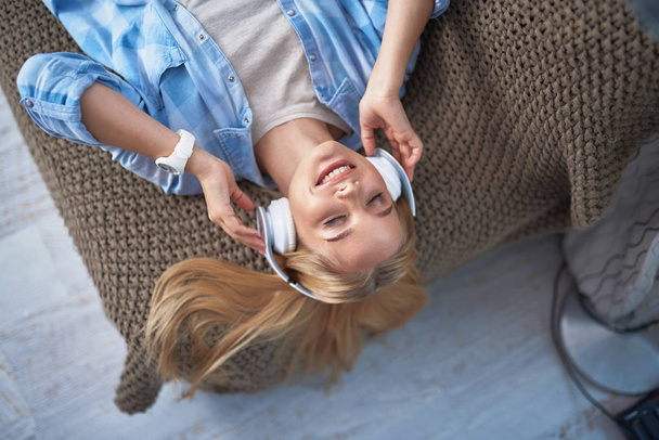 Charming young lady in blue shirt listening music at home - Foto, afbeelding