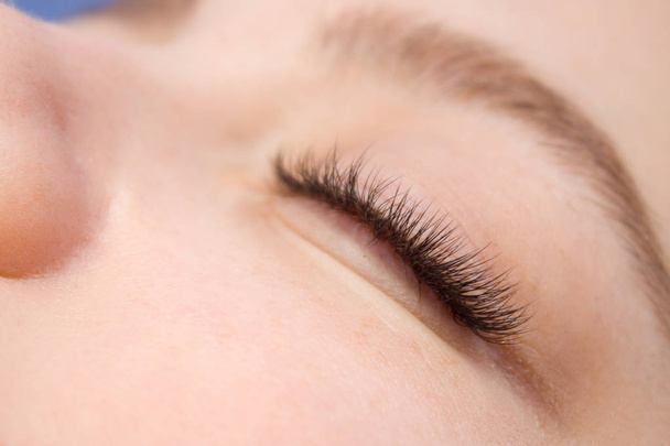 Eyelash Extension Procedure. Woman Eye with Long false Eyelashes. Close up macro shot of fashion eyes visagein in beauty salon. - Photo, Image