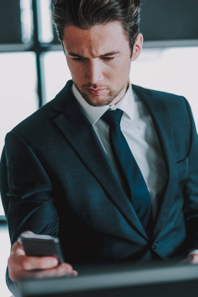 Calm man in elegant suit sitting and using his smartphone - Foto, afbeelding