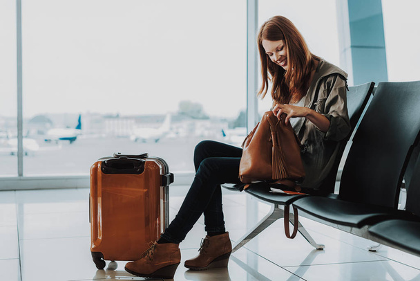 Smiling woman is waiting for flight with suitcase - Fotografie, Obrázek