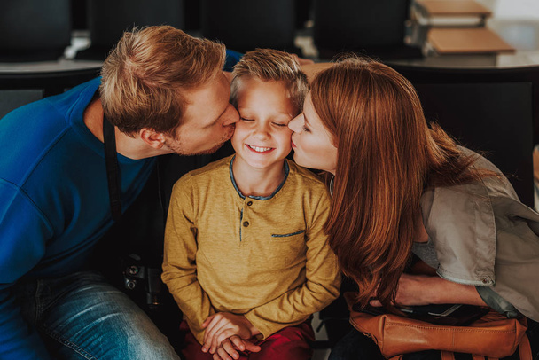 Caring parents are kissing their son in waiting hall - Foto, afbeelding