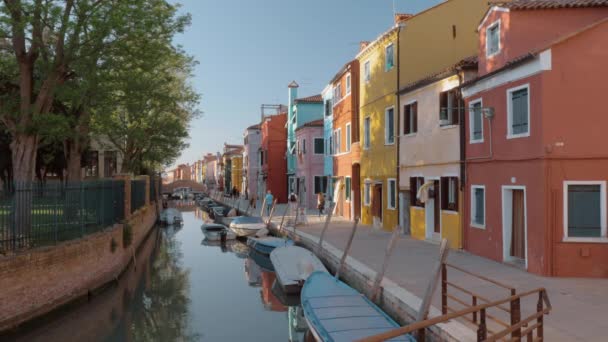 Waterside street with brightly painted houses and walking people. Burano, Italy - Footage, Video