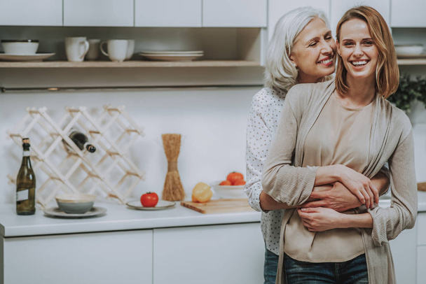 Happy aged woman is cuddling adult daughter at home - Foto, Bild
