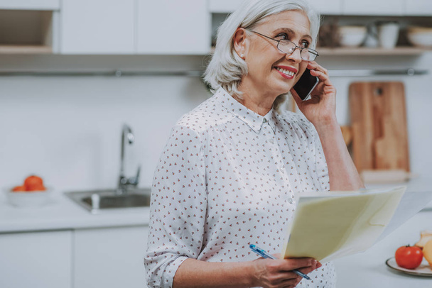 Smiling aged woman is communicating on phone at home - Photo, Image