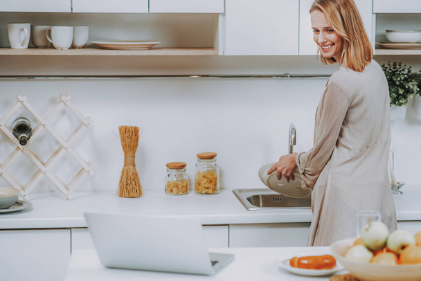 Cheerful woman is doing washing-up in kitchen - Foto, Bild
