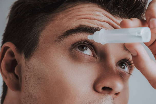 Close up of young man carefully using eye drops - Foto, afbeelding