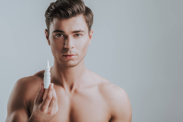 Handsome topless man holding nasal drops and looking calm - Photo, image