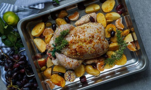 Baked turkey or juicy chicken with golden crispy skin with grapes and potatoes, tangerine. Roasted chicken in baking dish. Christmas dinner. Flat lay. Top view - Photo, Image