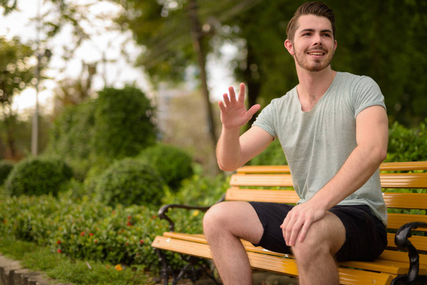 Muotokuva nuori komea mies istuu puistossa tervehtiessään
 - Valokuva, kuva