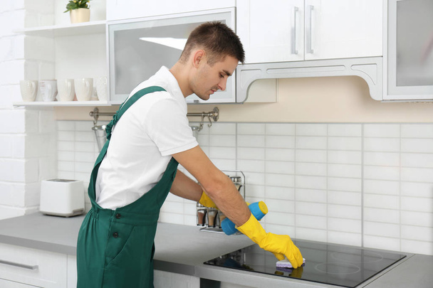 Male janitor cleaning kitchen stove with sponge in house - Foto, imagen