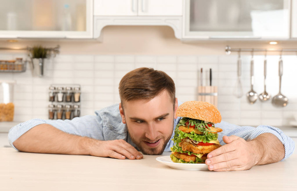 Young hungry man and huge burger on table - 写真・画像