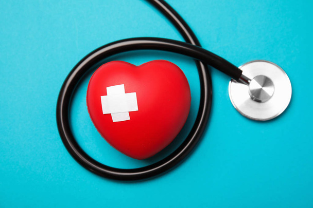 Stethoscope and red heart with adhesive plasters on color background, top view. Cardiology concept - Foto, afbeelding