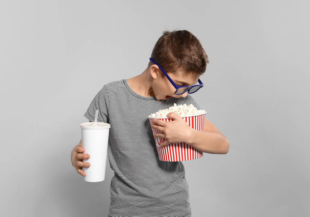 Boy with 3D glasses, popcorn and beverage during cinema show on grey background - Foto, imagen