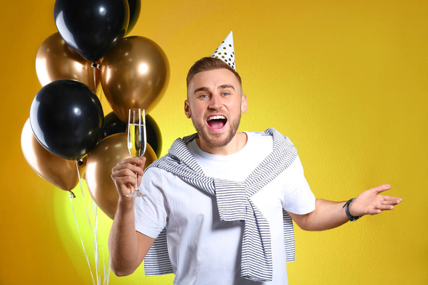 Portrait of happy man with champagne in glass and party balloons on color background - Foto, afbeelding